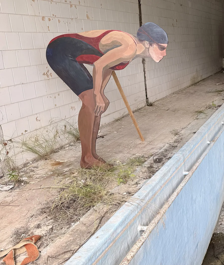 Side view of the freestanding swimmer installation on the overgrown tiled poolside.