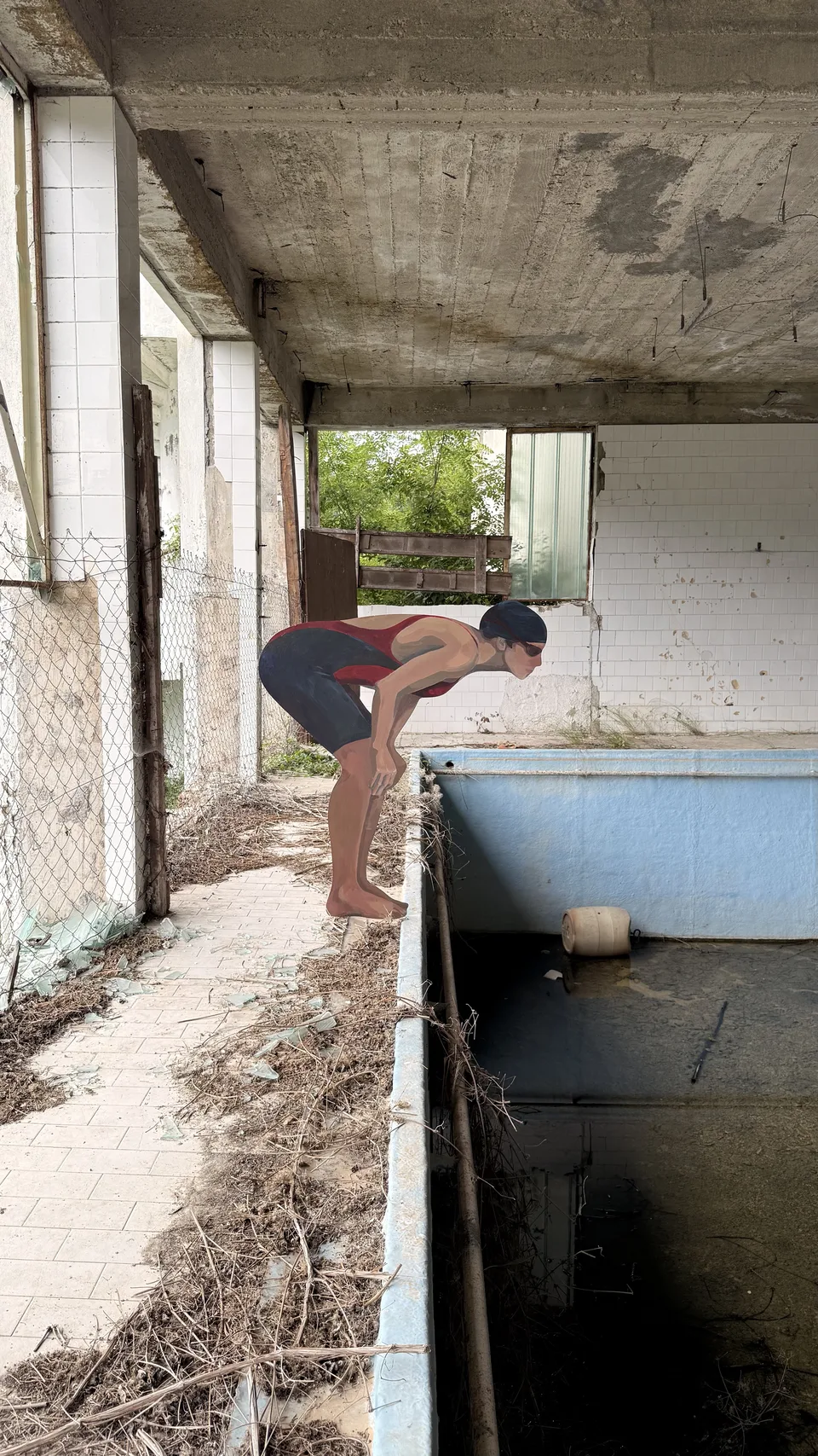 A painted swimmer poised over the edge of an abandoned pool, beneath a weathered concrete ceiling at Hotel Mir.